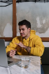 man in a yellow hoodie looking at his laptop